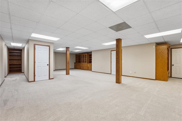 finished basement with baseboards, light colored carpet, and a drop ceiling