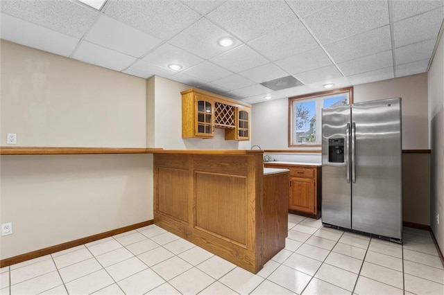 kitchen featuring brown cabinets, stainless steel fridge, a peninsula, baseboards, and glass insert cabinets