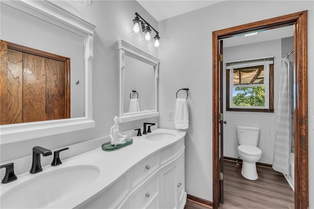 bathroom featuring wood finished floors, toilet, double vanity, and baseboards