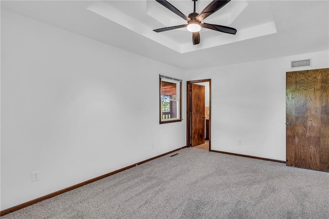 empty room with a tray ceiling, baseboards, carpet, and a ceiling fan