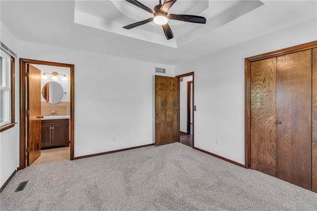 unfurnished bedroom featuring a sink, light carpet, baseboards, and a raised ceiling