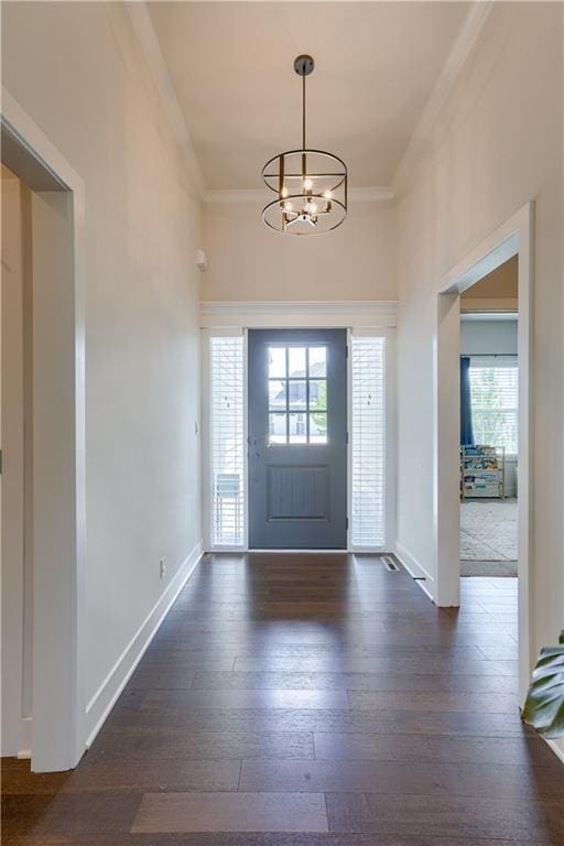 foyer entrance featuring crown molding, a chandelier, healthy amount of natural light, and dark wood-style flooring
