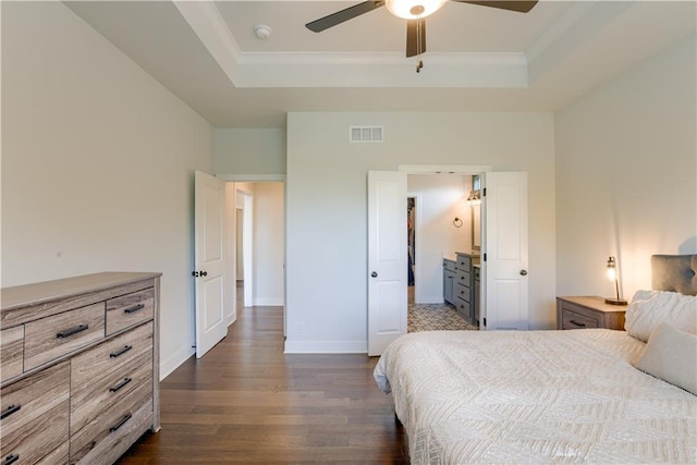 bedroom featuring a raised ceiling, dark wood finished floors, ornamental molding, baseboards, and ensuite bath