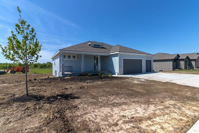 view of front of property with covered porch, an attached garage, driveway, board and batten siding, and a shingled roof