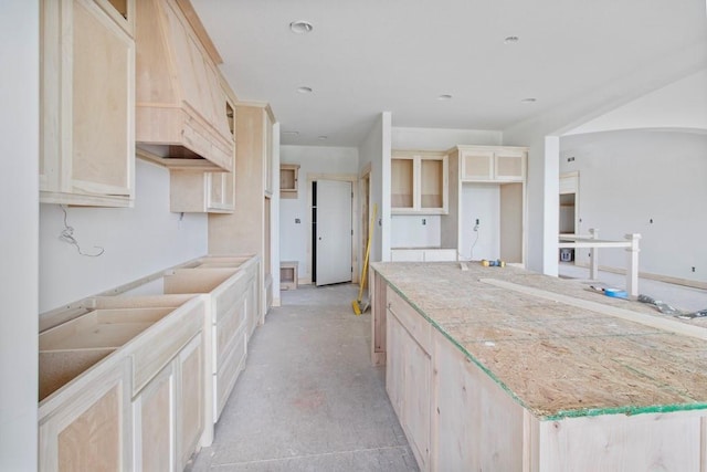 kitchen with light brown cabinetry, a large island, unfinished concrete flooring, and light stone countertops