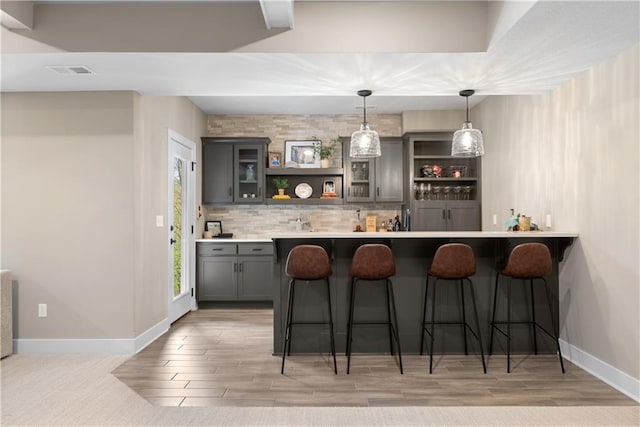5566 Thousand Oaks Dr, Parkville, MO 64152 - bar with pendant lighting, visible vents, light wood-style floors, baseboards, and backsplash