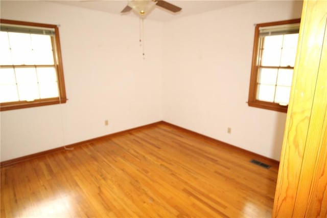 empty room featuring visible vents, a ceiling fan, light wood-style flooring, and plenty of natural light