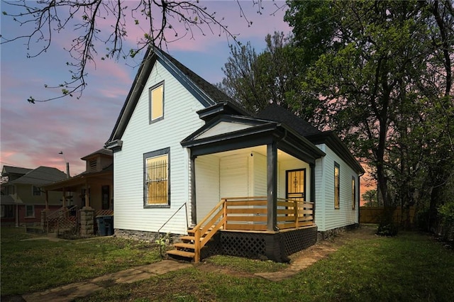 back of property at dusk with a porch, a lawn, and fence