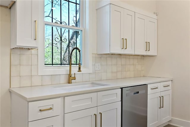 kitchen with stainless steel dishwasher, tasteful backsplash, a sink, light countertops, and white cabinetry