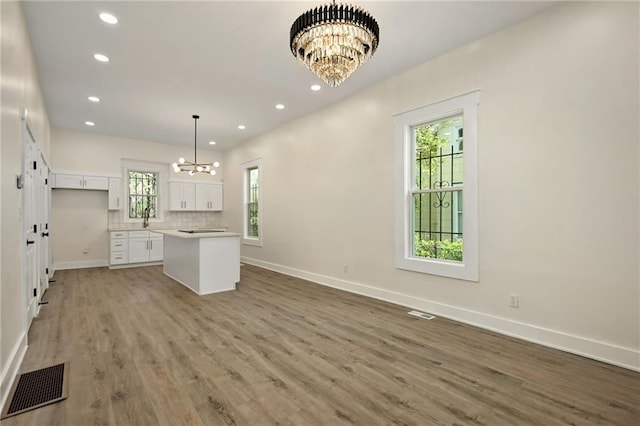 kitchen featuring a center island, white cabinets, baseboards, a notable chandelier, and visible vents