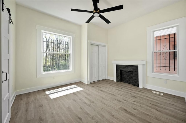 unfurnished living room with a ceiling fan, wood finished floors, a fireplace, baseboards, and visible vents