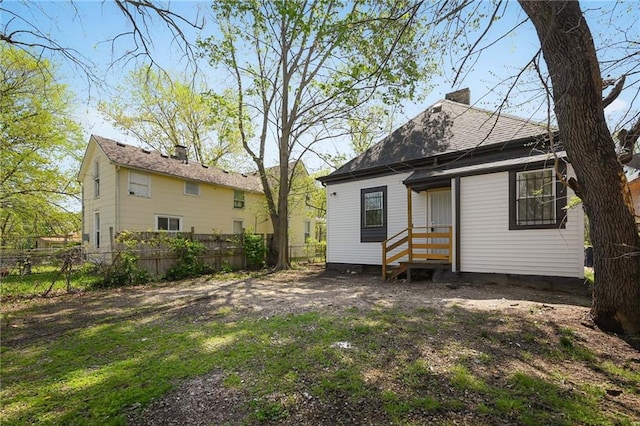 rear view of property featuring fence, a chimney, and roof with shingles