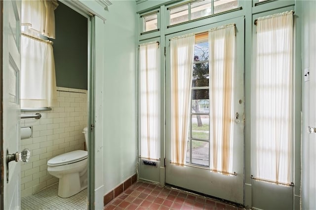 interior space with dark tile patterned floors, a wealth of natural light, a wainscoted wall, and tile walls
