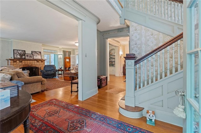 living area with stairs, crown molding, a brick fireplace, and wood finished floors