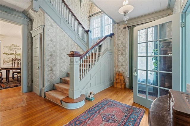 stairway featuring a wealth of natural light, crown molding, wood finished floors, and wallpapered walls