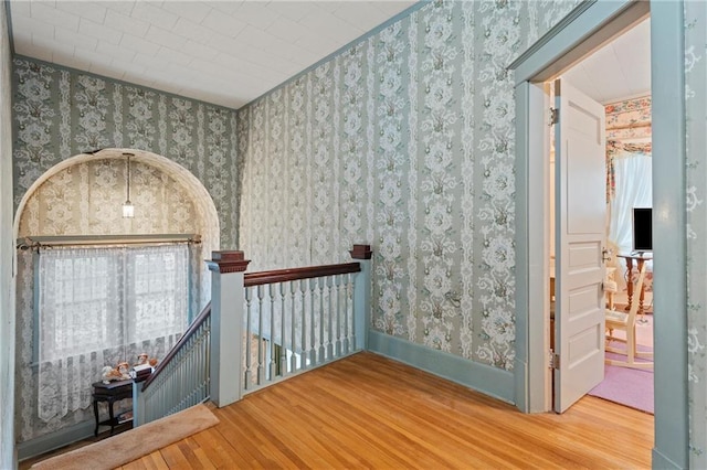 corridor with an upstairs landing, baseboards, wood finished floors, and wallpapered walls