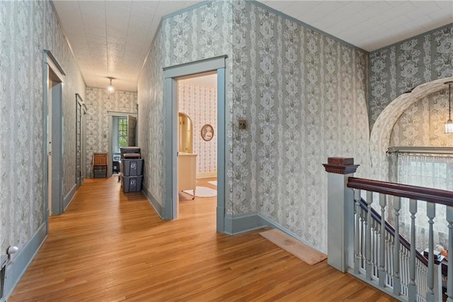 hall featuring wallpapered walls, wood finished floors, baseboards, and an upstairs landing