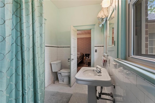 ensuite bathroom featuring a sink, tile walls, a wainscoted wall, toilet, and tile patterned flooring