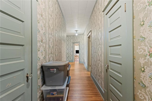 corridor featuring dark wood-style floors, baseboards, and wallpapered walls