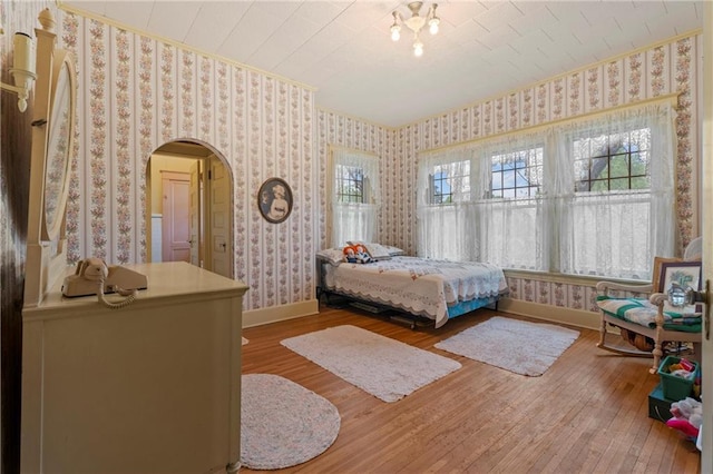 bedroom with wallpapered walls, hardwood / wood-style flooring, baseboards, and arched walkways