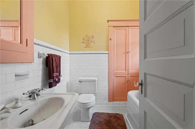 bathroom featuring a sink, toilet, tile walls, wainscoting, and tile patterned flooring