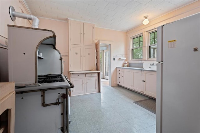 kitchen featuring light floors, crown molding, white cabinetry, and freestanding refrigerator