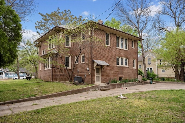 view of front facade with a front lawn, a chimney, brick siding, and central air condition unit