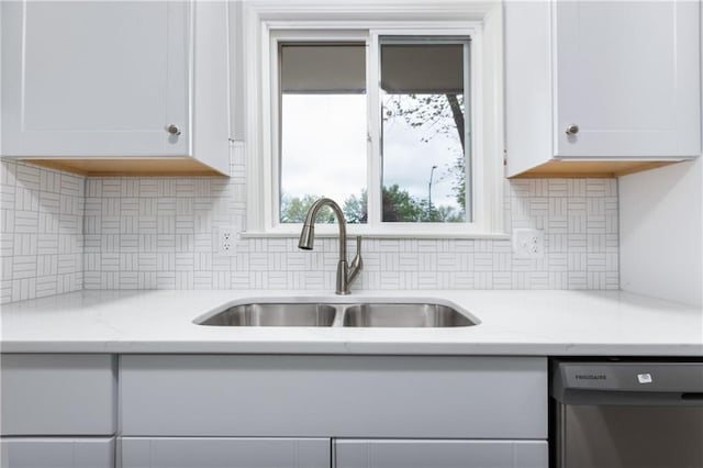 kitchen featuring white cabinetry, tasteful backsplash, a sink, dishwashing machine, and light stone countertops