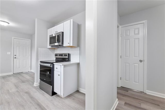 kitchen with tasteful backsplash, white cabinets, appliances with stainless steel finishes, light countertops, and light wood finished floors