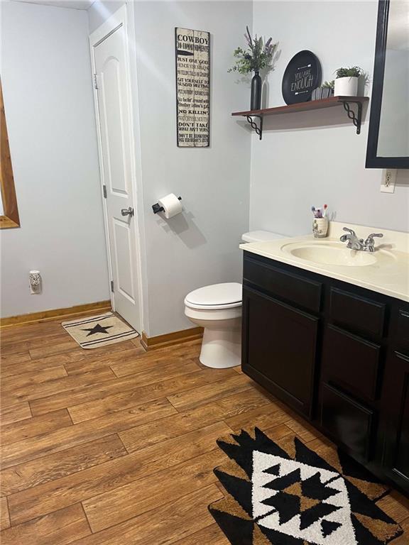 bathroom with wood finished floors, toilet, vanity, and baseboards