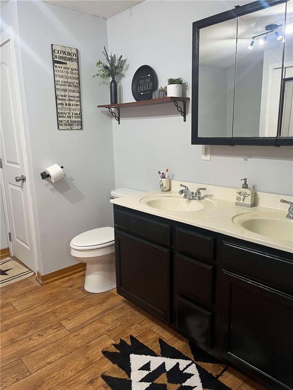 full bathroom featuring double vanity, wood finished floors, toilet, and a sink