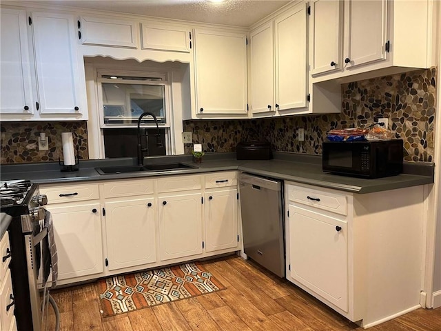 kitchen with white cabinets, a sink, appliances with stainless steel finishes, dark countertops, and light wood-type flooring