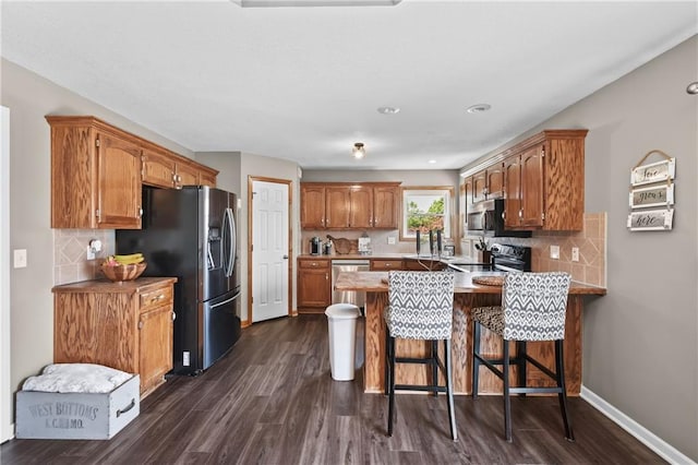 12200 E 214th Ter, Peculiar, MO 64078 - kitchen with appliances with stainless steel finishes, a peninsula, decorative backsplash, dark wood-style floors, and recessed lighting