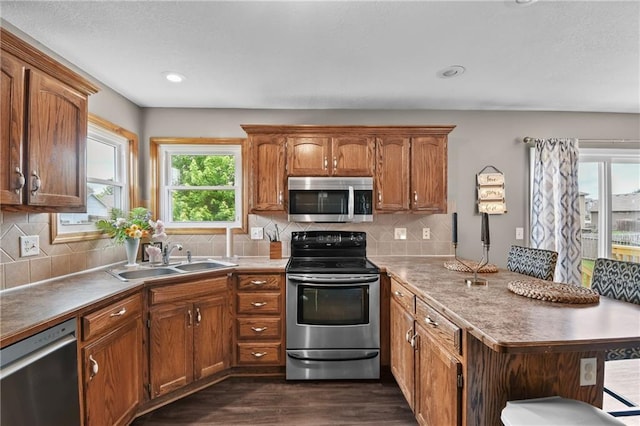 12200 E 214th Ter, Peculiar, MO 64078 - kitchen with stainless steel appliances, a sink, a peninsula, dark wood-style floors, and brown cabinets