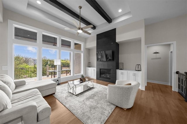 6309 NW 58th Ter, Kansas City, MO 64151 - living room featuring baseboards, beamed ceiling, wood finished floors, ceiling fan, and a fireplace