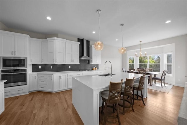 6309 NW 58th Ter, Kansas City, MO 64151 - kitchen with stainless steel appliances, an inviting chandelier, light countertops, wall chimney range hood, and a sink