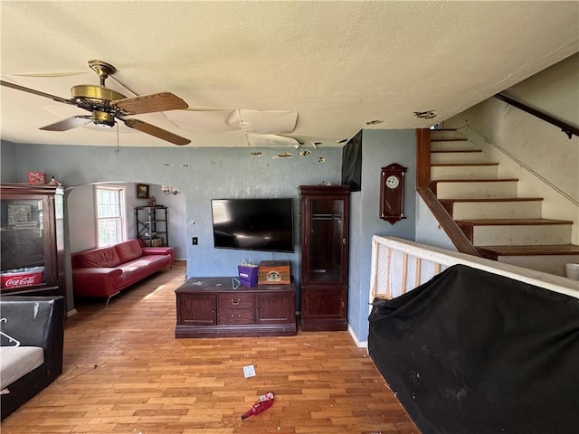 living room featuring a ceiling fan, stairway, light wood finished floors, and a textured ceiling