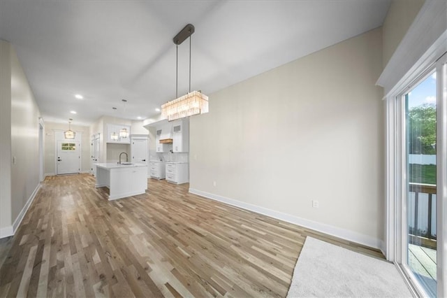 unfurnished living room featuring baseboards, a sink, light wood finished floors, and recessed lighting