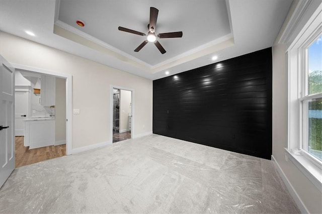 unfurnished bedroom featuring a raised ceiling, ornamental molding, light carpet, baseboards, and recessed lighting