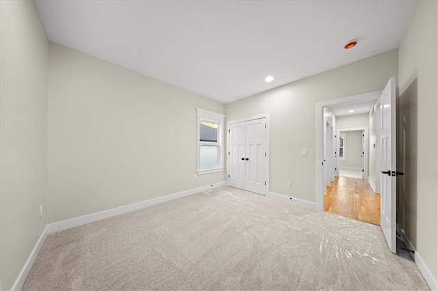 unfurnished bedroom featuring light colored carpet, baseboards, recessed lighting, and a closet