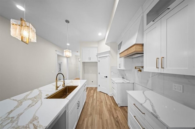 kitchen with light stone countertops, a sink, light wood-type flooring, white cabinetry, and decorative light fixtures