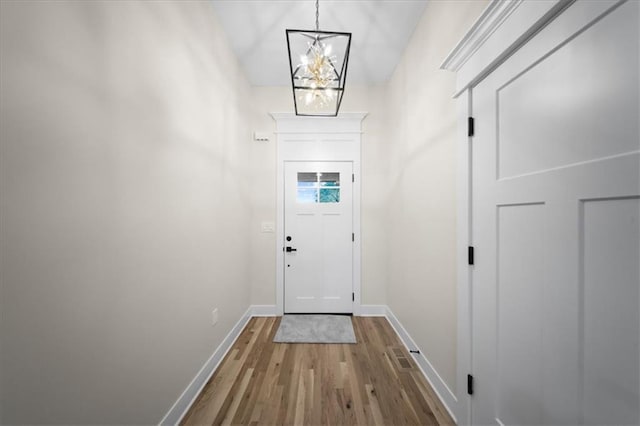 doorway to outside with a chandelier, wood finished floors, and baseboards