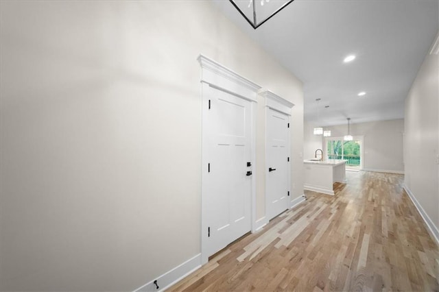 hall with light wood-style flooring, recessed lighting, baseboards, and a sink