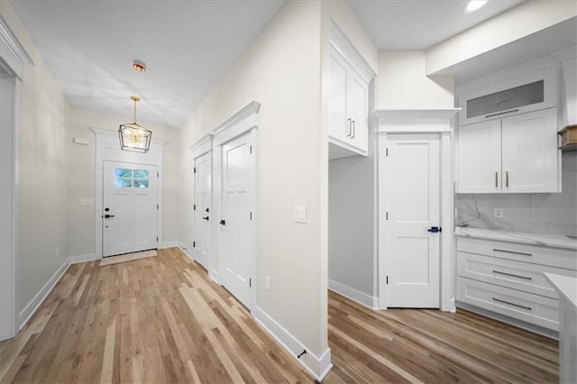 entryway featuring light wood-type flooring, a chandelier, and baseboards