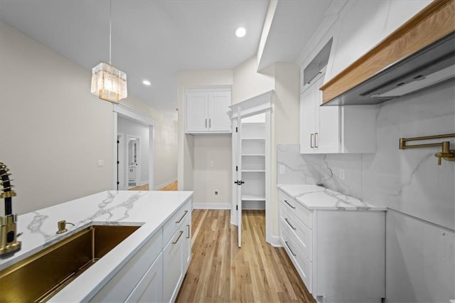 kitchen with custom range hood, white cabinetry, light stone counters, light wood finished floors, and pendant lighting