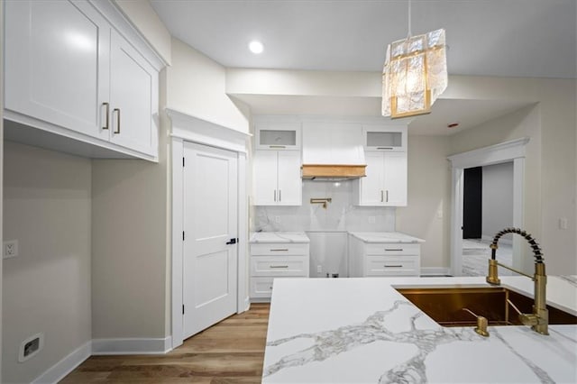 kitchen featuring a sink, light stone counters, white cabinetry, glass insert cabinets, and wood finished floors