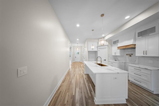 kitchen featuring custom range hood, wood finished floors, baseboards, a sink, and white cabinets