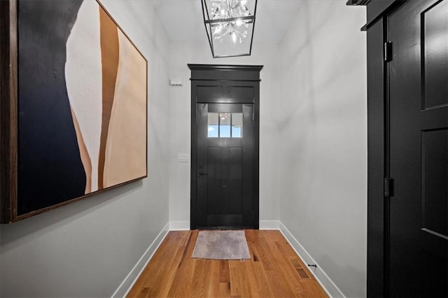 doorway to outside featuring baseboards, a chandelier, and wood finished floors