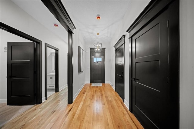 hallway with baseboards, light wood-type flooring, and a chandelier