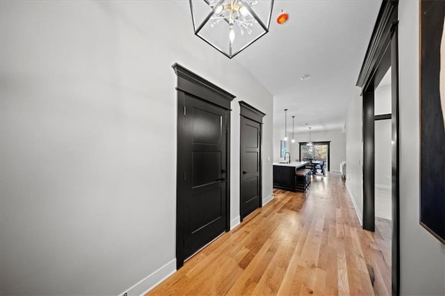 hallway with baseboards, light wood-style floors, and a sink